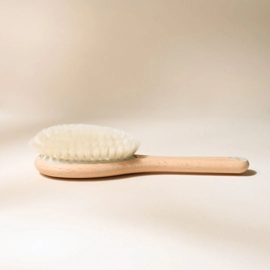Bachca baby hair brush on a beige background, natural beechwood with ultra-soft bristles, photographed close-up from the side.