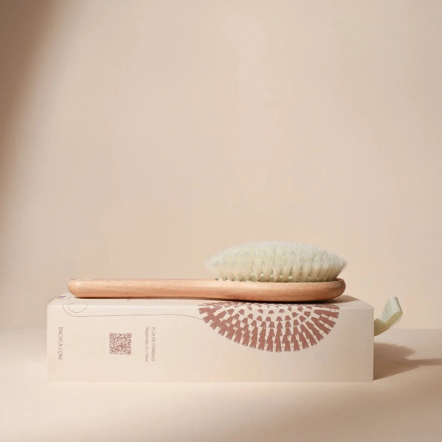 Bachca baby hair brush on its case, natural wood handle and ultra-soft white bristles, photographed on a beige background for a clean and soothing look.