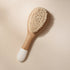 Small Bachca baby hair brush with soft goat hair bristles and a wooden handle, photographed on a pale pink background.