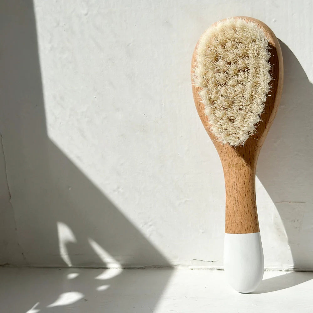 Bachca baby hair brush with goat hair bristles, positioned vertically on a white windowsill.