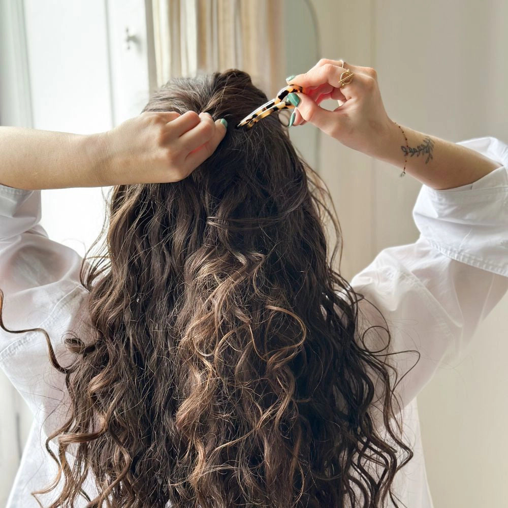 Person styling another person's hair with a clip in a well-lit room.