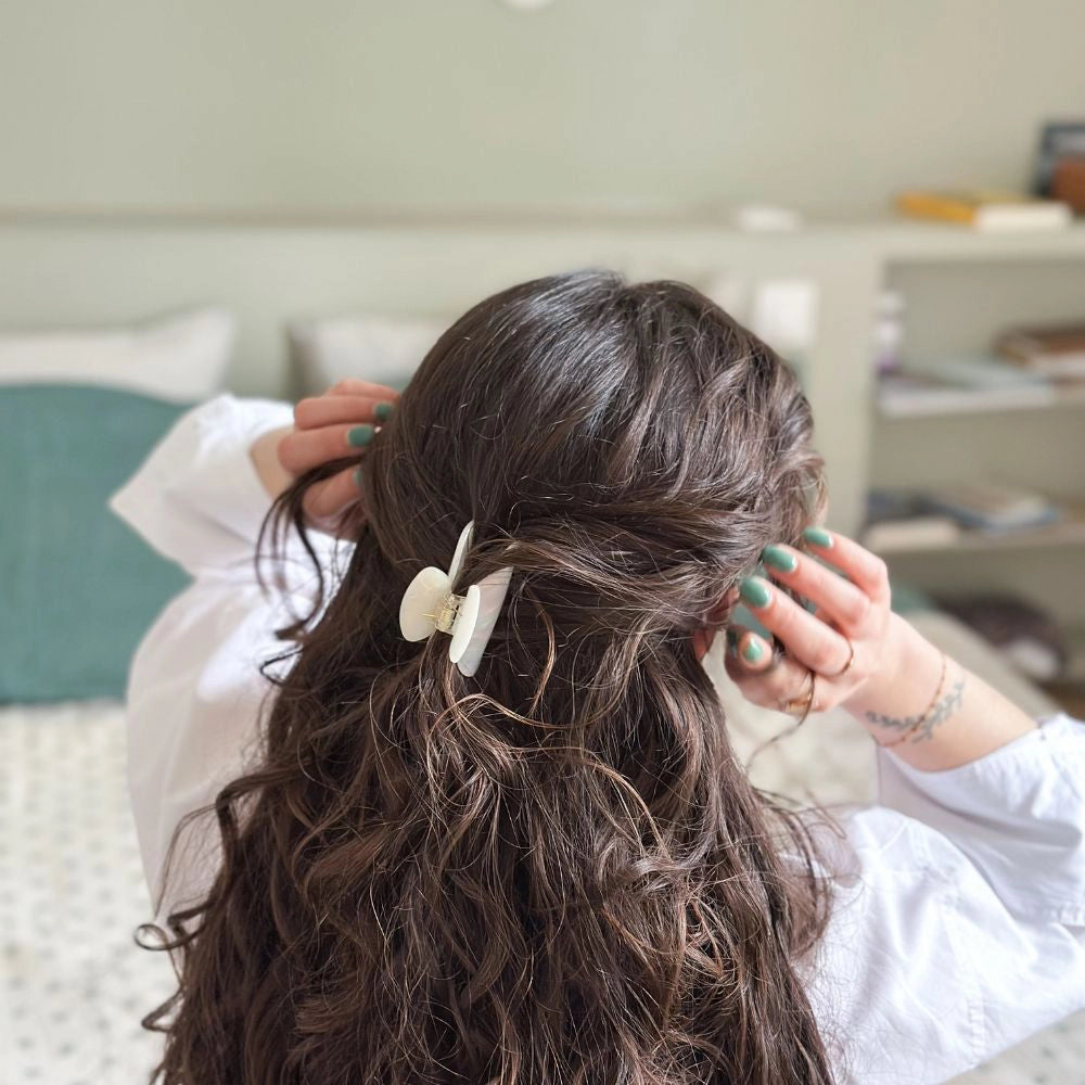 Person styling their hair with pearly hair claw clip in classic in a casual indoor setting