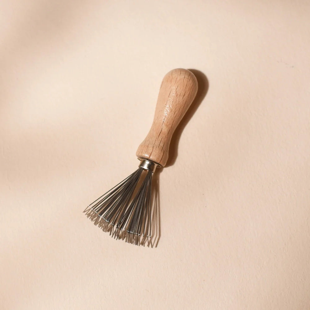 Bachca metal and wood cleaning comb, perfect for maintaining your hairbrushes. Displayed on a soft pink background.
