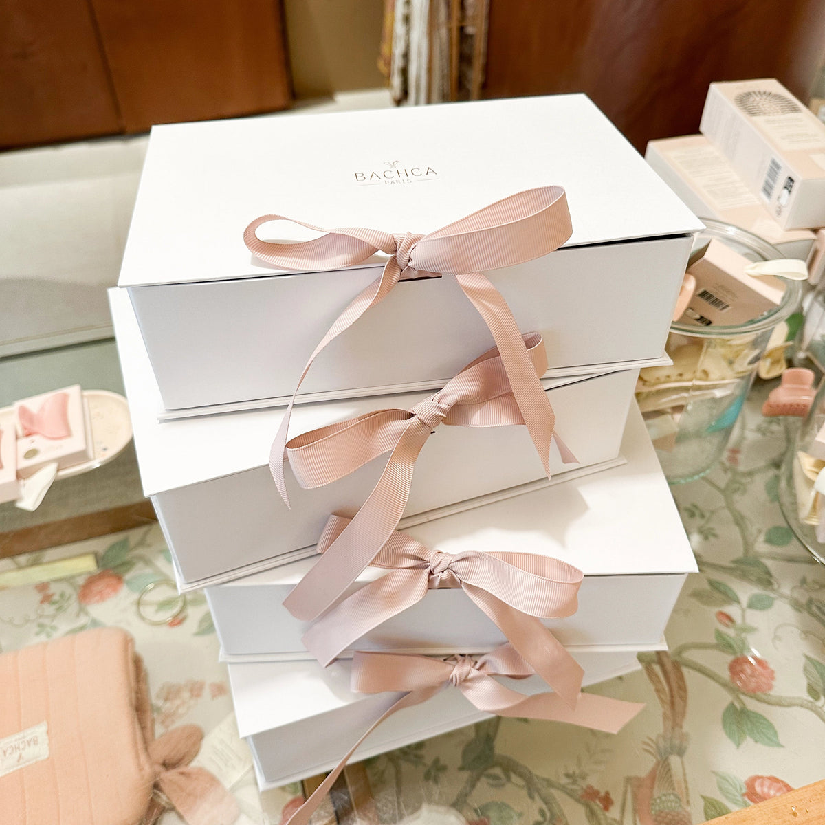 Stack of white boxes with pink ribbons on a floral-patterned surface