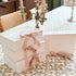 Stack of white boxes with pink ribbons on a floral tablecloth, with a candelabra in the background.
