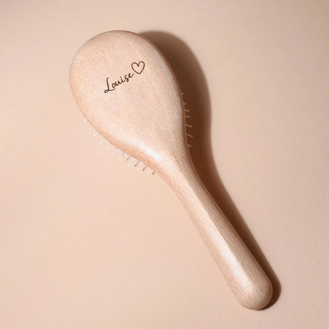 Bachca hairbrush in light beechwood, personalized with the name “Louise” and a small heart engraved on the back, placed on a soft beige background.