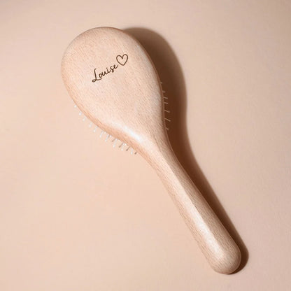 Bachca hairbrush in light beechwood, personalized with the name “Louise” and a small heart engraved on the back, placed on a soft beige background.