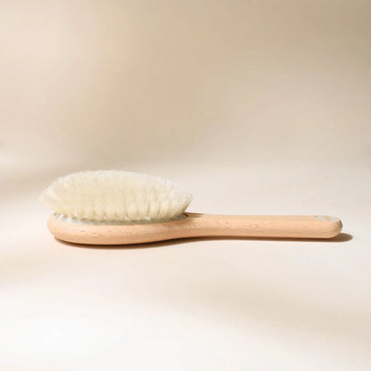 Bachca baby hair brush on a beige background, natural beechwood with ultra-soft bristles, photographed close-up from the side.