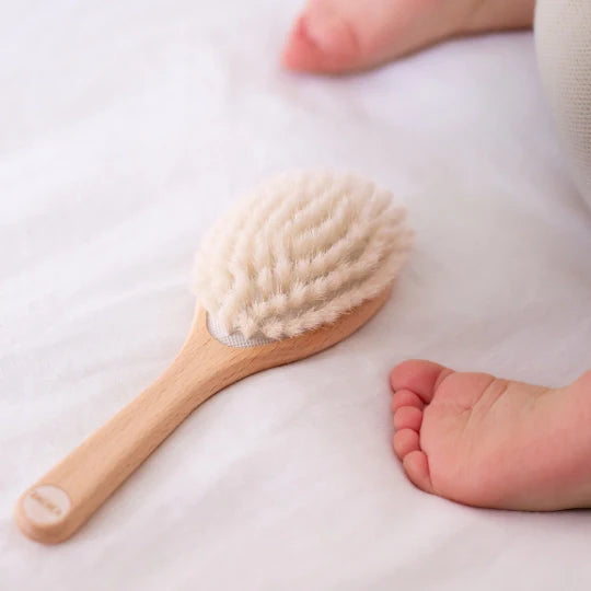 Bachca baby hair brush placed on a white sheet near a newborn’s feet, with ultra-soft bristles and a beechwood handle, perfect for gentle styling from birth.