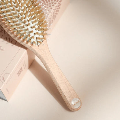 Close-up of the Bachca hair brush, light wood handle engraved, placed on its blush pink box, highlighting the details of the nylon and boar bristles.