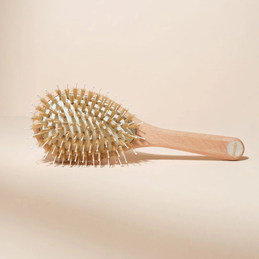 Small Bachca hair brush, top view, showing boar and nylon bristles, beechwood handle with pearlescent medallion, placed on a uniform beige background.