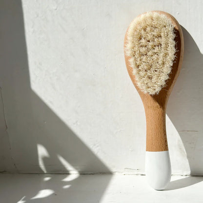 Bachca baby hair brush with goat hair bristles, positioned vertically on a white windowsill.