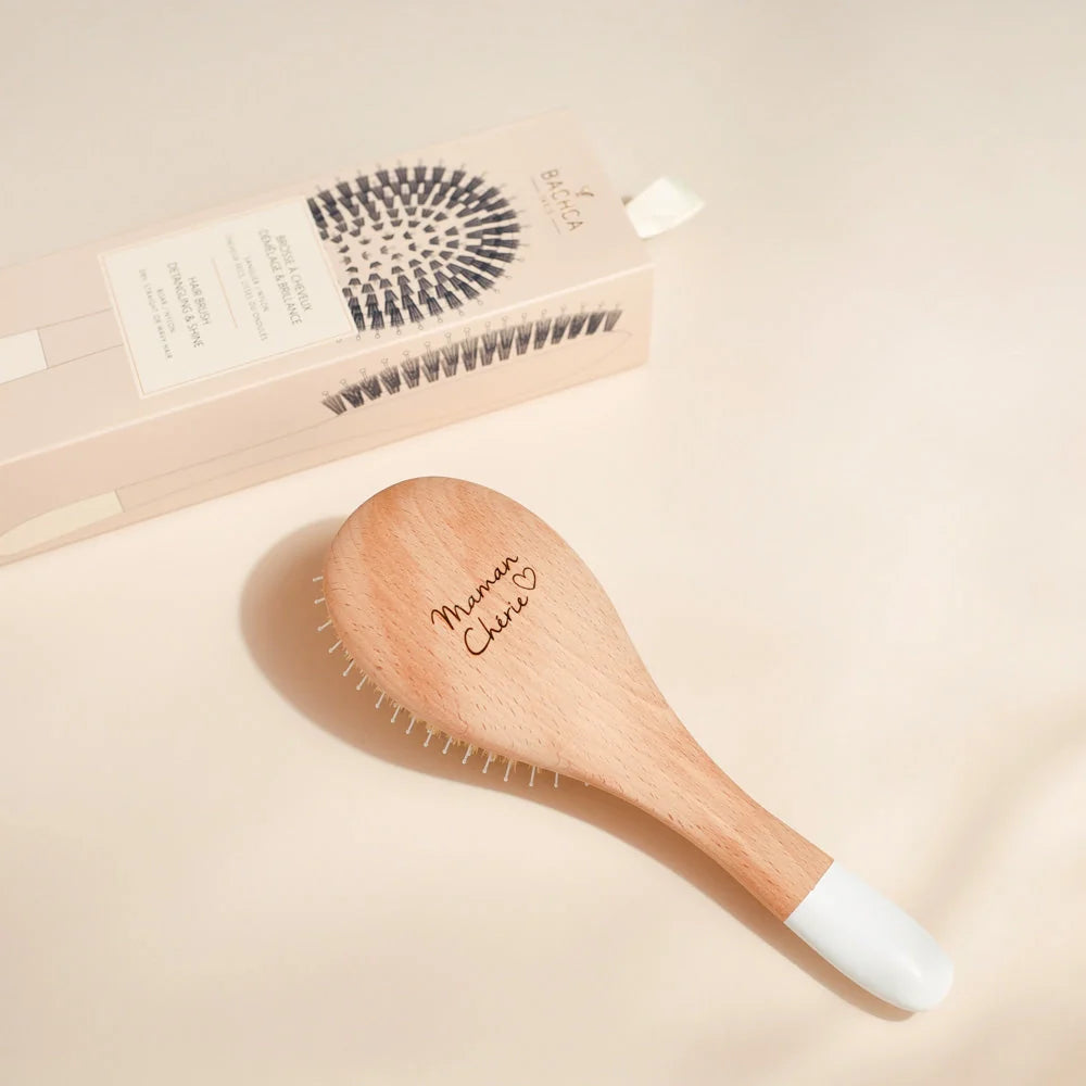 Bachca Gloss and Detangling Hair brush with its bristles facing down and the bottom of the brush upright where we see a Maman Cherie engraving with a heart 