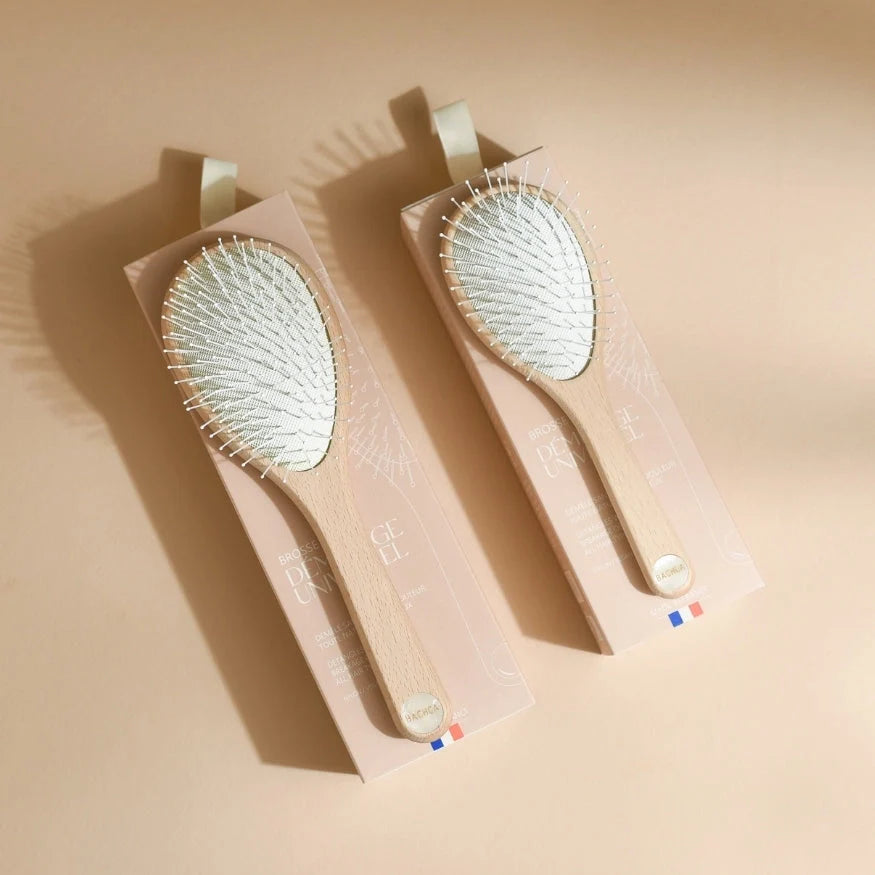 Duo of Bachca Everyday Detangling Hair Brushes presented in their blush pink boxes, with light wood handles and white bristle cushions, laid flat on a beige background with a defined shadow.