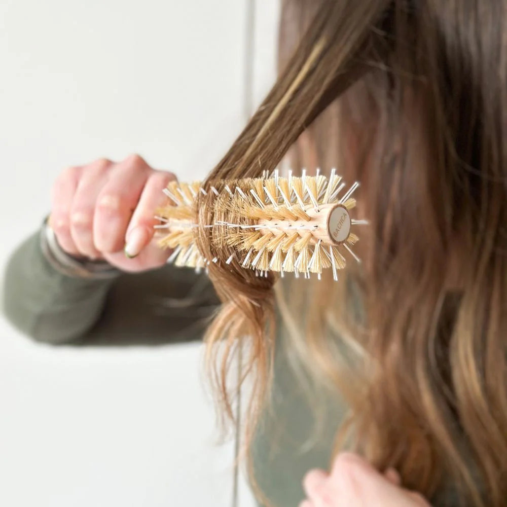 Styling hair with the Bachca round brush in natural wood, featuring mixed bristles for smoothing and styling.