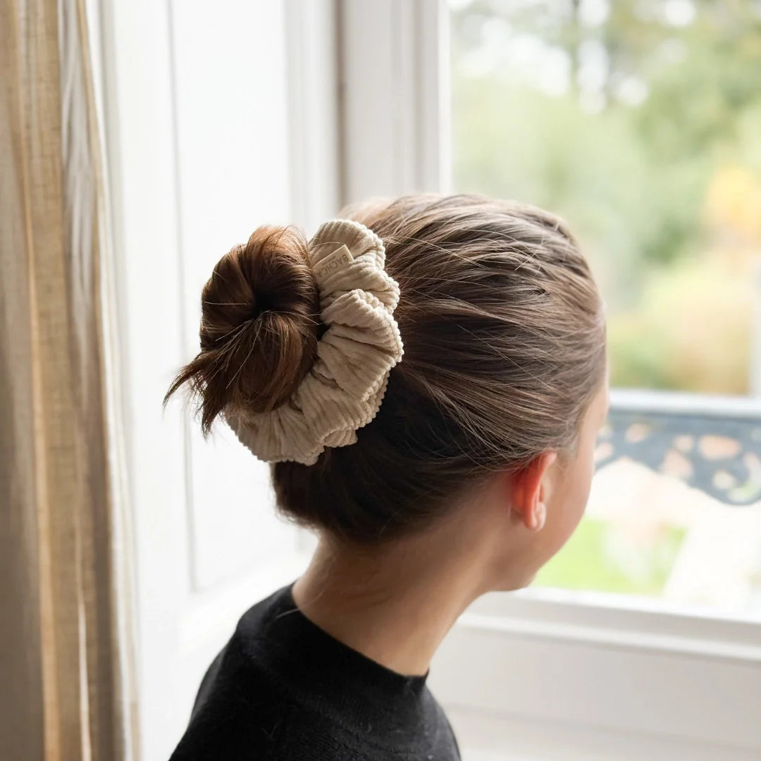 Bachca beige ribbed velvet scrunchie worn in a messy bun, back view indoors.