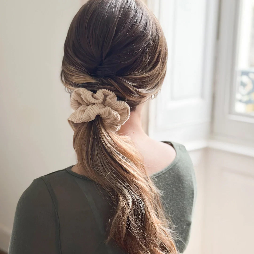 Bachca beige ribbed velvet scrunchie securing a low ponytail, hairstyle viewed from the back.