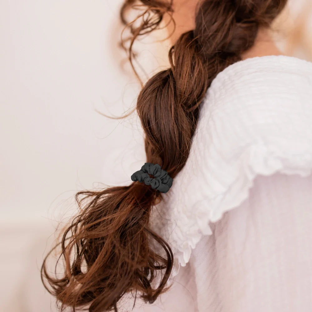 Bachca silk scrunchie holding a long, soft braid on brunette hair, worn by a young girl in a white blouse with a ruffled collar.