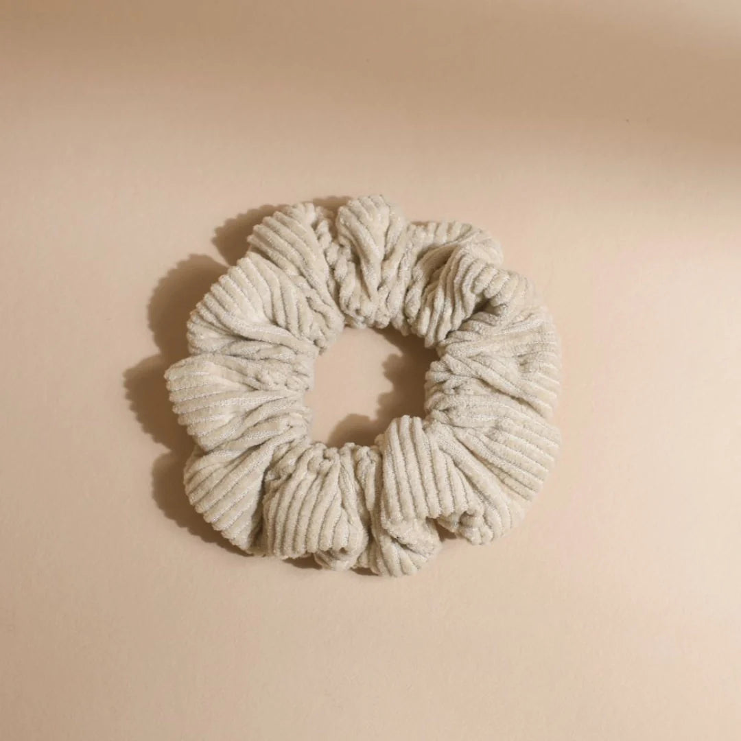Bachca beige ribbed velvet scrunchie, photographed flat on a soft sandy background.