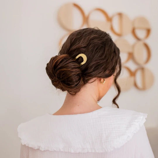 Elegant low bun held in place with a gold Bachca chignon pin, in a soft, natural setting