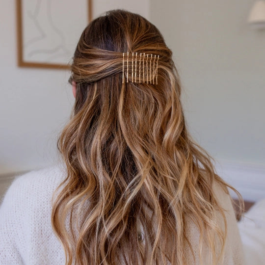 Person with blonde wavy hair wearing a gold bobby pins in a neutral indoor setting