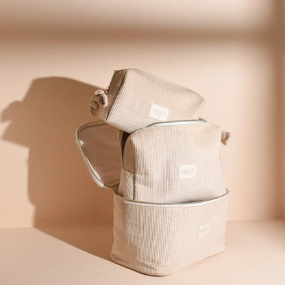 Collection of BACHCA sand velvet toiletry bags stacked in a vanity, bright cream background.