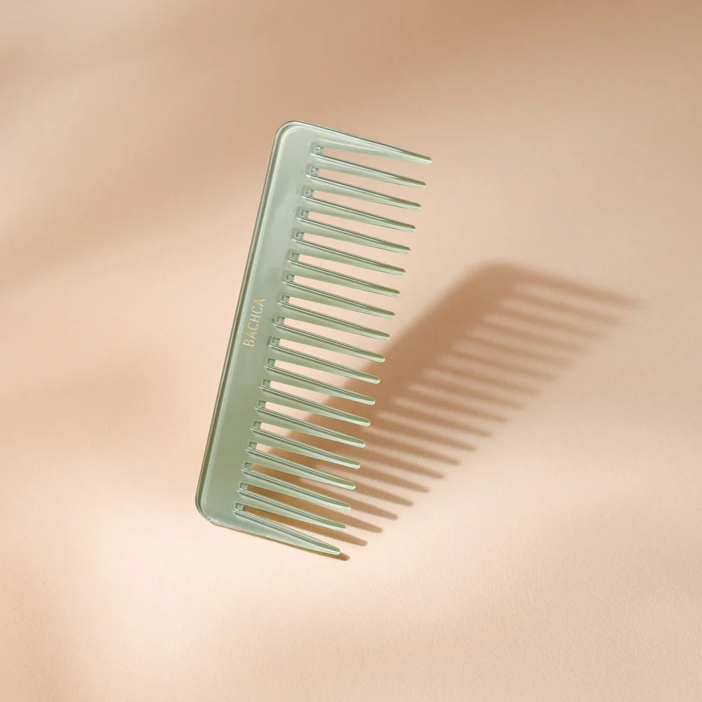 Seafoam green acetate hair comb with wide, spaced teeth, signed by Bachca, presented against a pale pink background.