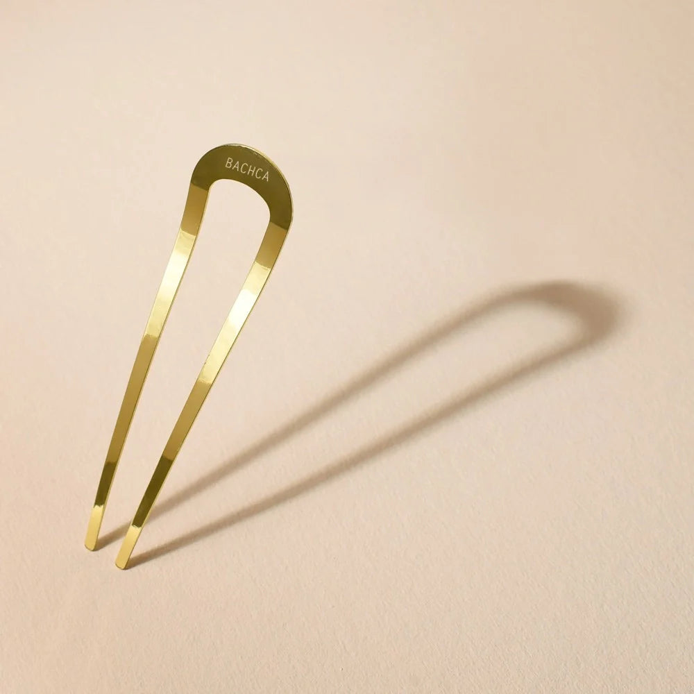 Grand chignon pin in gold metal by Bachca, displayed on a pale pink background