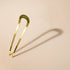 Grand chignon pin in gold metal by Bachca, displayed on a pale pink background