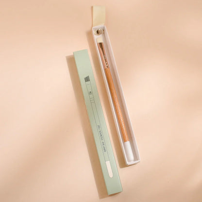 Woman applying eyeshadow with a Bachca brush featuring a wooden handle, concentrating on her upper eyelid makeup, in natural light.