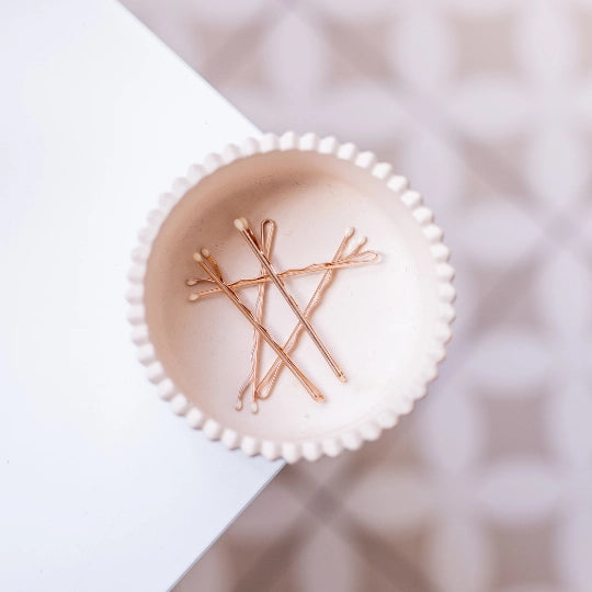 Rose gold hair pins on a white ceramic plate with a blurred background