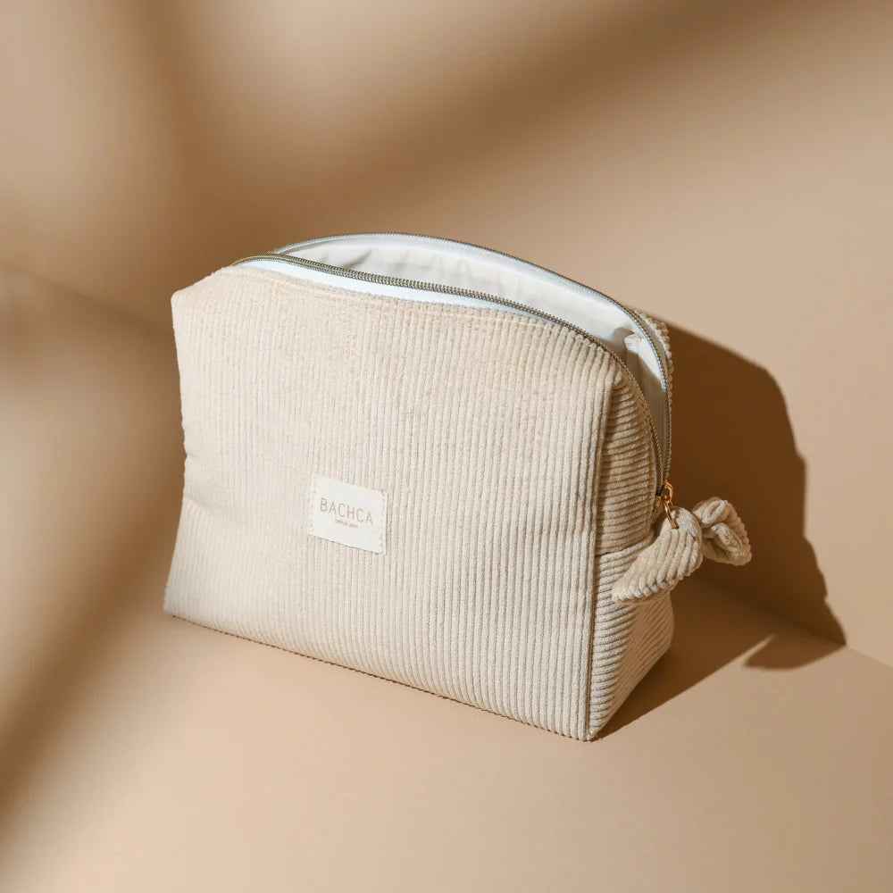 BACHCA sand velvet toiletry bag, placed on a sandy surface, bathed in gentle natural light.