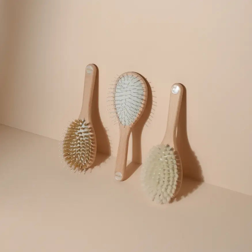Three wooden Made in France Bachca collection hairbrushes with light natural wood handles and soft bristles in beige, white, and pale blue tones, arranged on a minimalist beige surface against a matching background.